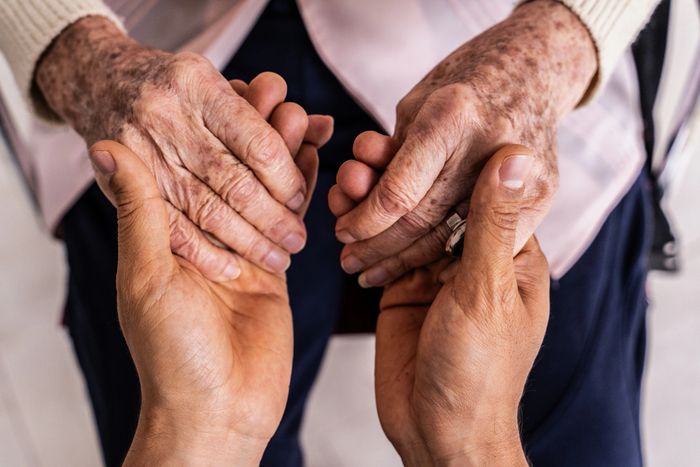 Younger hands gently holding elderly hands in a comforting gesture.
