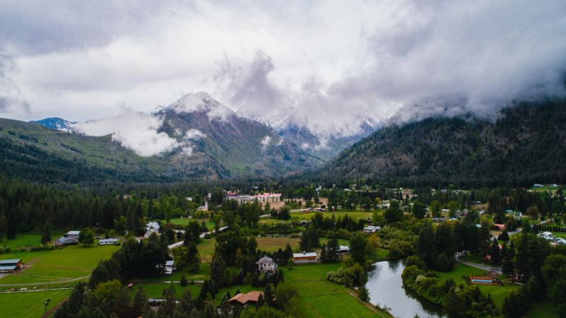 Scenic aerial view of Leavenworth, Washington on a cloudy, Spring day, surrounded by evergreen forests and with snowcapped mountains visible in the distance.