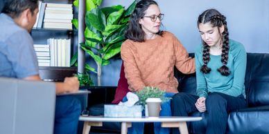 A woman comforts a distressed teenage girl during therapy.
