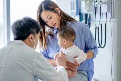 Doctor examining a baby held by the mother in a clinic.