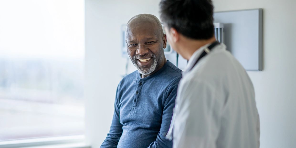 A smiling elderly man talking with a doctor in a bright clinic room.