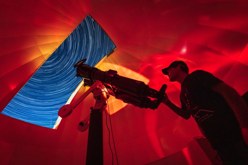 Astronomer in photo telescope dome with red light checking settings