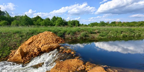 A small waterfall flowing into a calm pond under a blue sky.