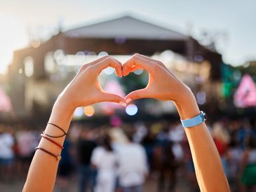 Hands forming a heart shape at an outdoor concert during sunset.