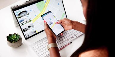 Person using a smartphone and laptop to browse maps and real estate listings.