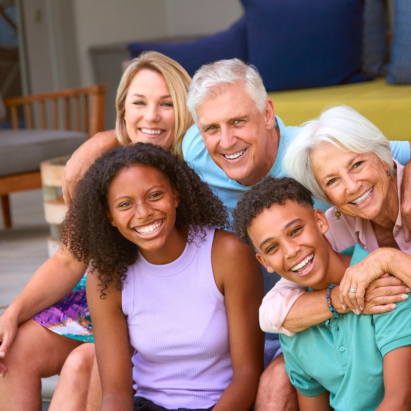 Portrait Of Three Generation Family Laughing And Smiling Sitting Outdoors At Home On Deck Together