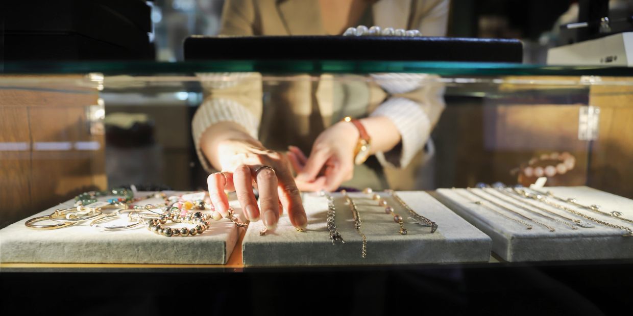 Person selecting jewelry behind glass display.