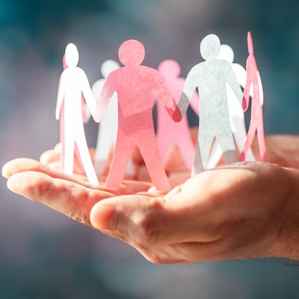 Paper cutout figures holding hands resting on an open palm.