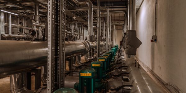 Industrial room with rows of green pumps and stainless steel pipes.