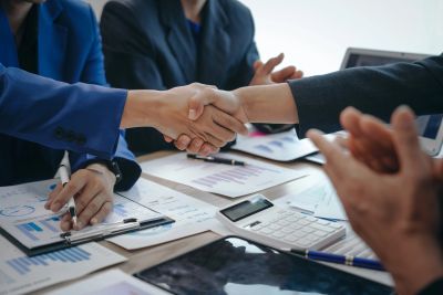 Two businesspeople shaking hands over a desk with documents.