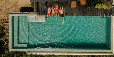 Family of four relaxing beside a clear blue pool on a sunny day.