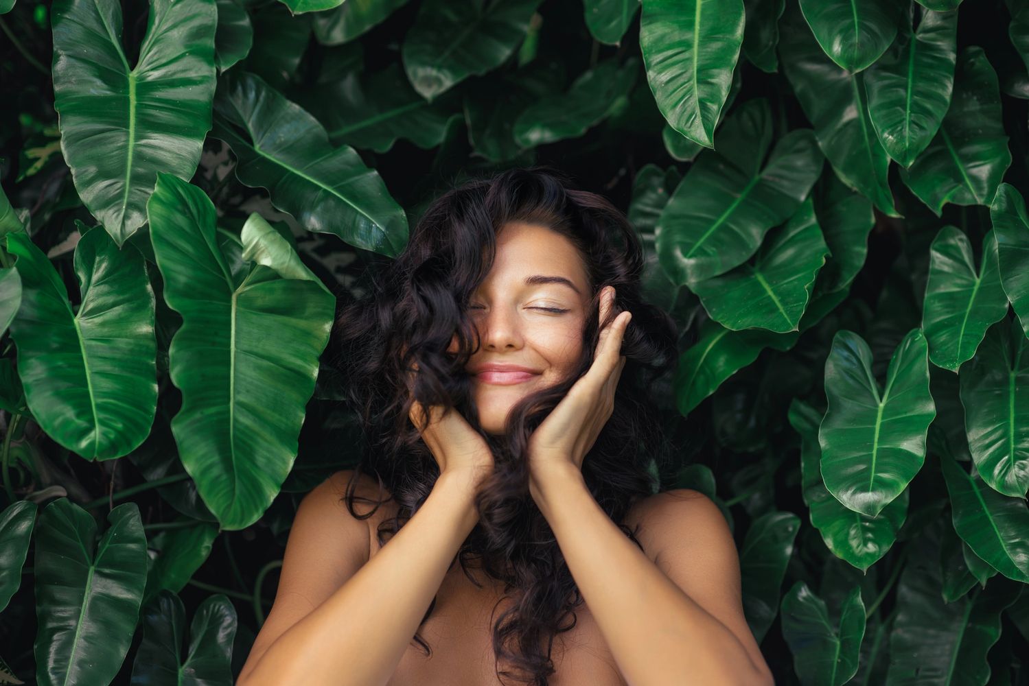 Woman with closed eyes smiling amid lush green leaves. nextgen Miami, nextgen therapy, services offered by nexgen health and wellness