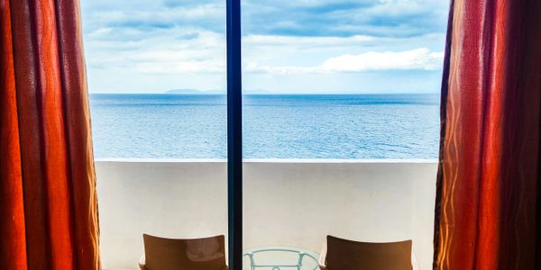 Balcony view of the ocean framed by orange curtains and two chairs.