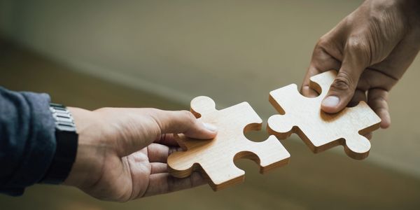 Two hands holding wooden puzzle pieces about to connect.