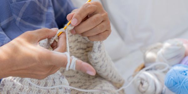 Hands crocheting with white yarn and a yellow hook.