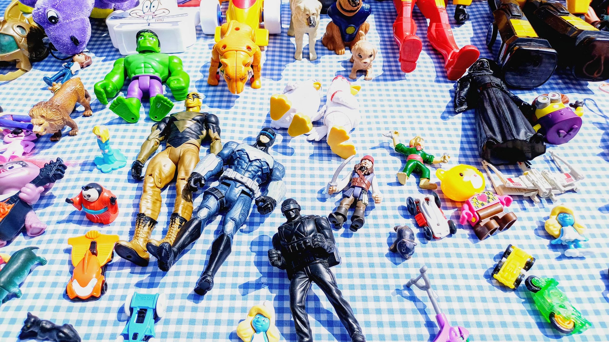 A colorful assortment of toys and action figures on a checkered cloth.