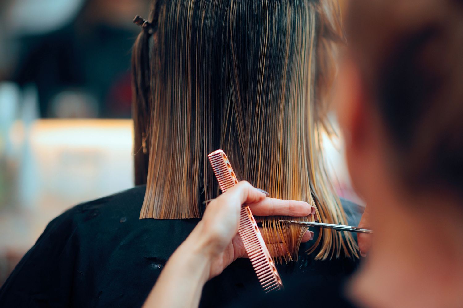 A woman cutting her hair with scissors and comb.