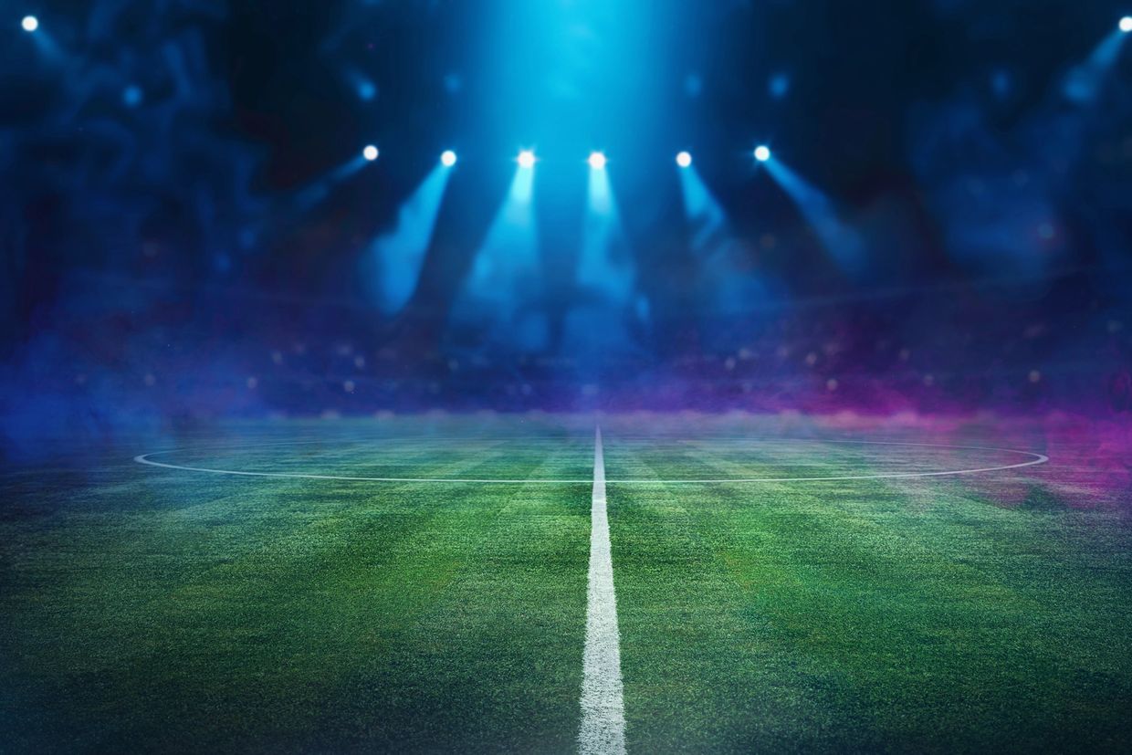 Empty football field illuminated by bright stadium lights at night.