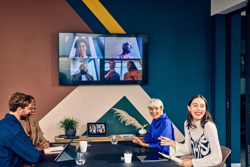 Team members in a modern office engaging with remote colleagues via a video conference call. Hybrid work environment and digital communication concept