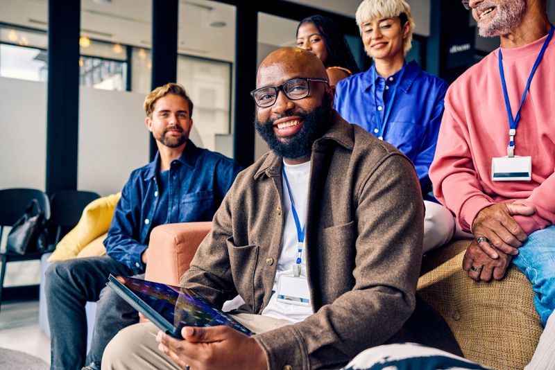 Smiling African American businessman using a tablet in a team meeting at a modern office. Technology integration and teamwork in business concept for design and print.