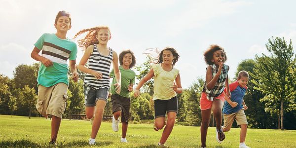 Six children running joyfully on a sunny grassy field.