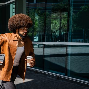 Man with afro hairstyle holding coffee and tablet, walking confidently outdoors.