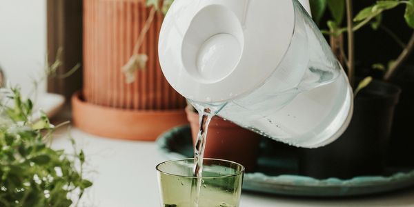 Pouring water from a white pitcher into a green glass on a white table.