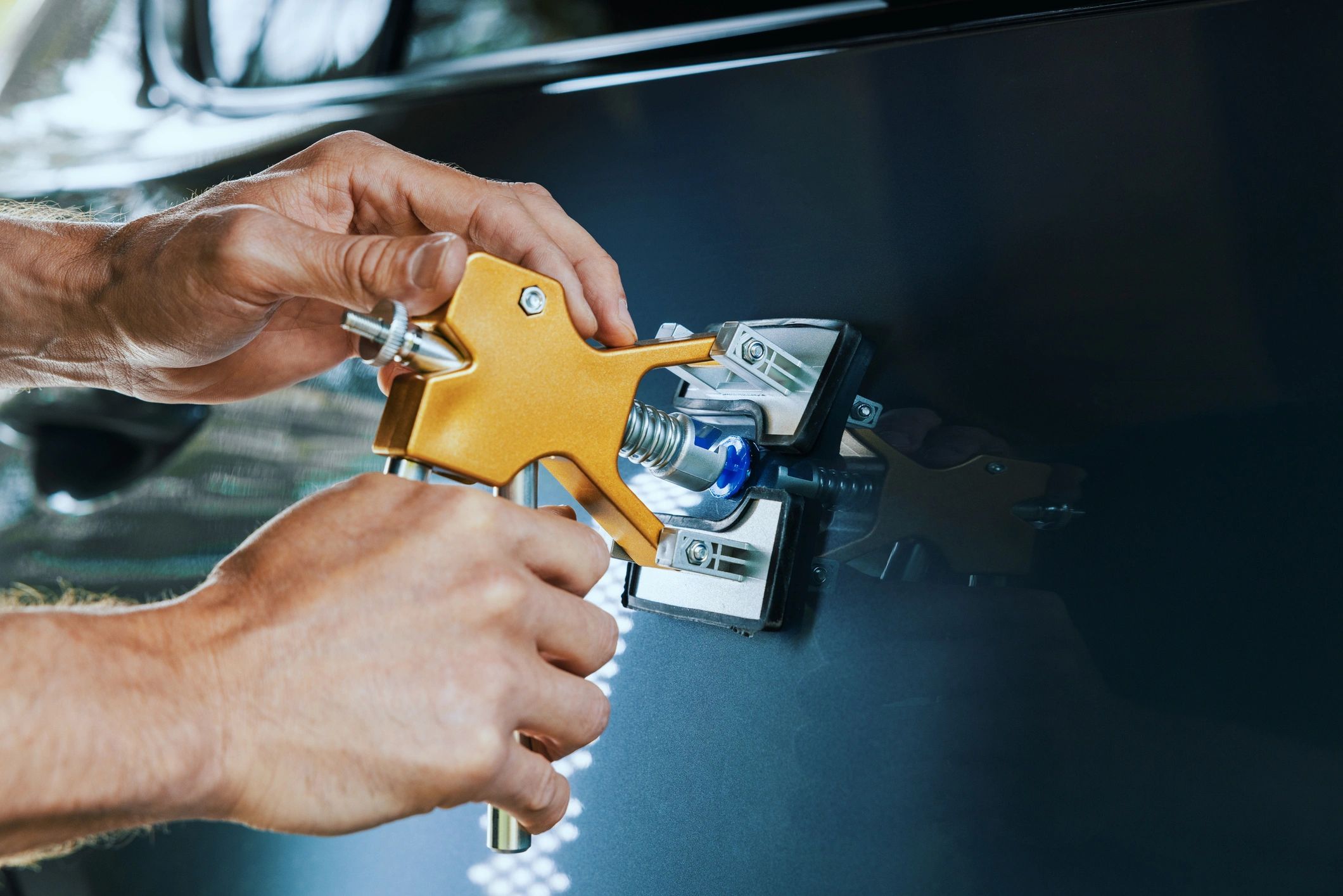 Hands using a tool to fix a dent on a car's surface.