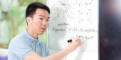 A man explains mathematical eigenvalues and equations on a whiteboard.