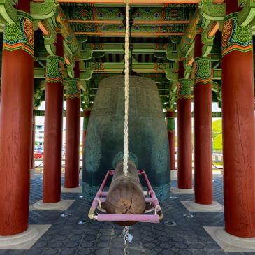 Traditional large bell with a wooden striker in a decorated pavilion.