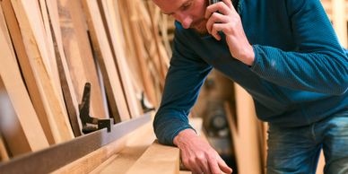 A man inspecting wood in a workshop while talking on the phone.