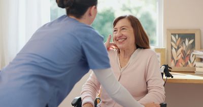 A nurse smiling and interacting with an elderly woman in a wheelchair.