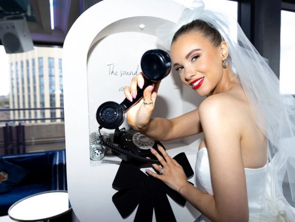 A bride in a wedding dress smiling while holding a vintage telephone receiver.