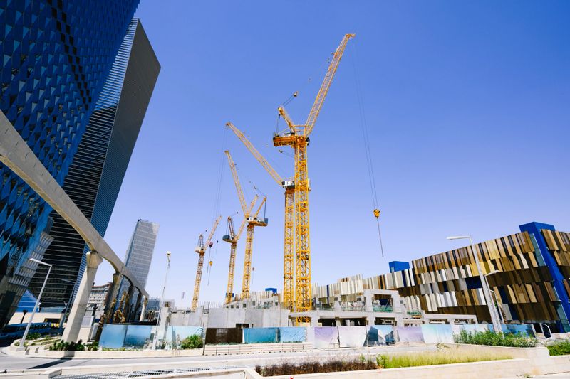 Five tower cranes surrounded by new structural development in Al Aqiq neighborhood of Riyadh, Saudi Arabia.