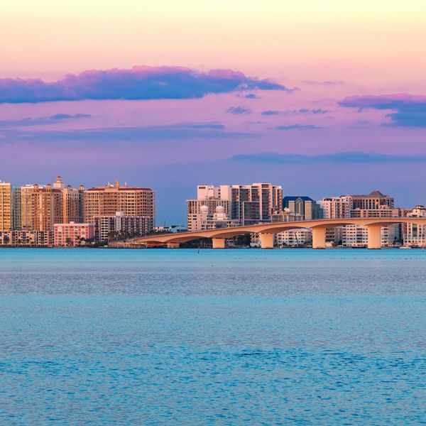 City skyline with a bridge over calm water at sunset.