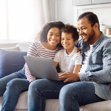 Happy family of three using a laptop together on a couch.