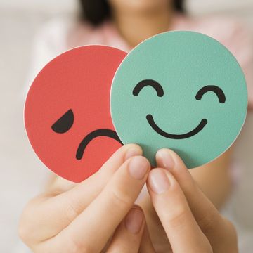 Hands holding paper cutouts of happy and sad faces, representing changing moods and emotions