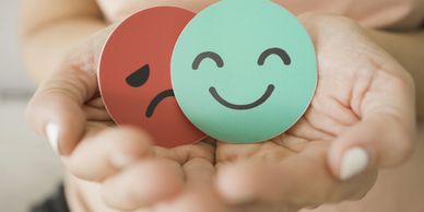 Hands holding happy and sad face emoticons symbolizing emotions.
