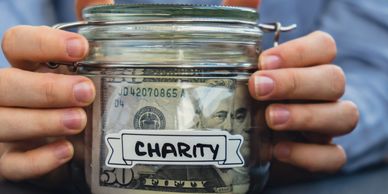 Hands holding a jar labeled 'Charity' filled with money.