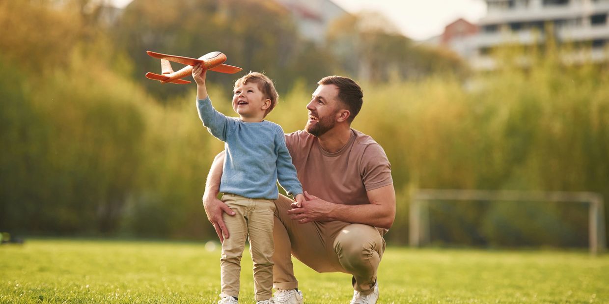 A father and a young son smiling and playing with each other outside.