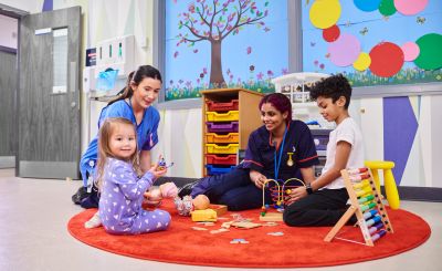 Children and caregivers playing on a round red rug.
