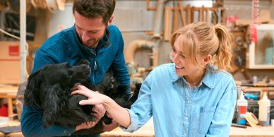Man and woman petting a black dog indoors.