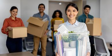 Smiling employees carrying boxes and office supplies during an office move.