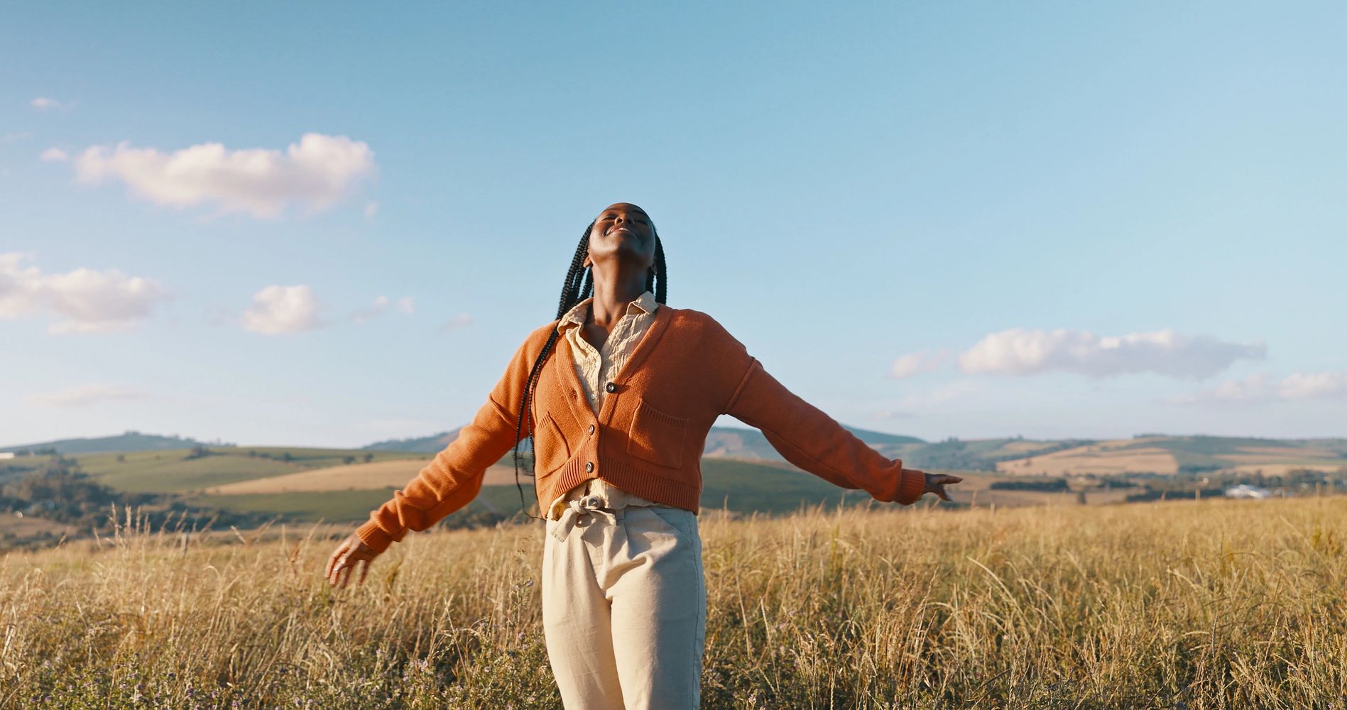Woman enjoying a sunny day in an open field, arms outstretched.