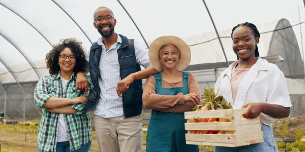 Four farmers smiling inside a greenhouse with fresh produce.