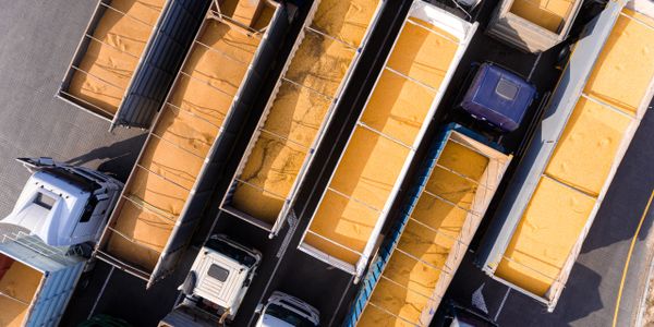 Aerial view of trucks loaded with yellow grain in a parking area.