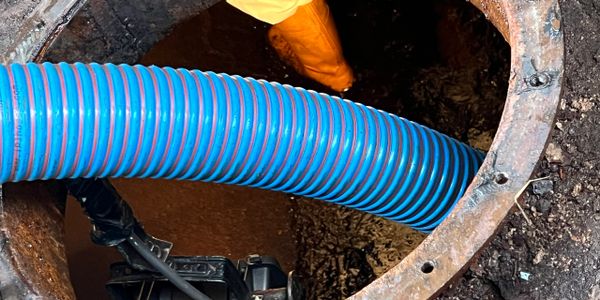 Workers using a large blue hose to clean a manhole.