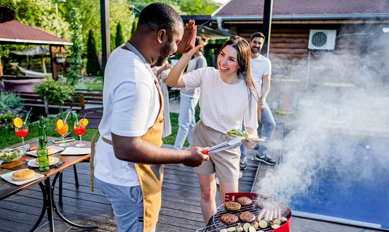 Friends having a barbecue pool party, a man with an apron grilling and giving meats to his friends
