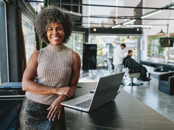 Woman smiling near laptop in a modern salon with a client getting a haircut.