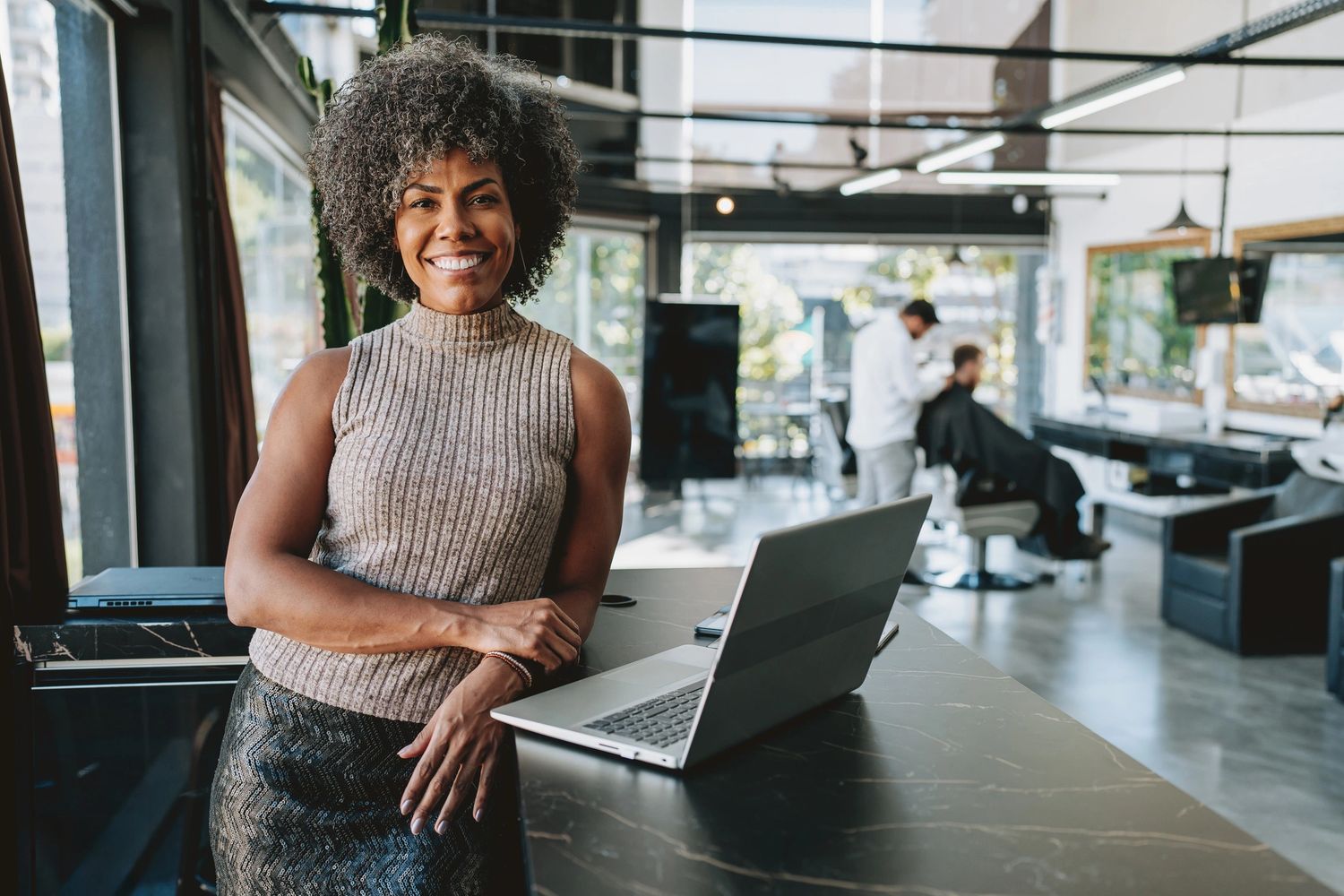 Smiling woman standing at a counter with a laptop in a modern salon.